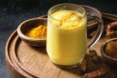 a glass mug filled with yellow liquid next to bowls of tumerical and ginger