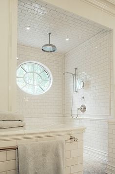 a bathroom with white tile walls and flooring next to a bathtub, shower head, and window