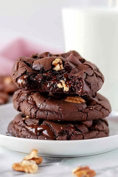 chocolate cookies stacked on top of each other next to a glass of milk and nuts