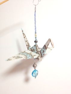 an origami bird hanging from a hook on a wall with beaded necklaces