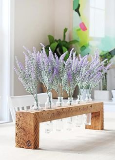 lavender flowers are arranged in glass vases on a wooden bench