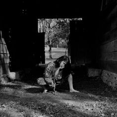 black and white photograph of a woman kneeling on the ground in front of a barn