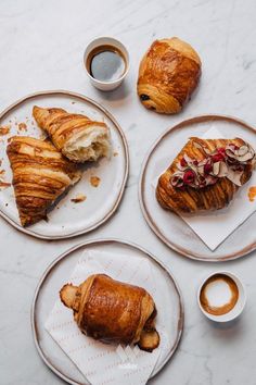 three croissants and two cups of coffee on plates