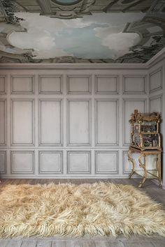 a room with a rug, chair and painting on the wall above it that has clouds painted on the ceiling