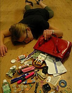 a woman laying on the floor with her purse and many other items scattered around it