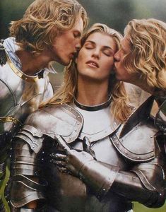 three people in armor kissing each other on the foreheads and chest, with one woman wearing