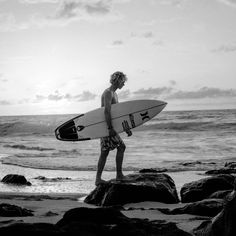 a young man holding a surfboard on top of a beach next to the ocean