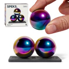 a hand is touching two shiny balls on a stand with the box next to it