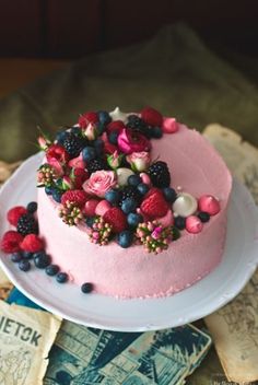 a pink cake with berries and blueberries on top is sitting on a white plate