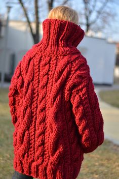 the back of a woman's red cabled cardigan sweater, with her hands in her pockets