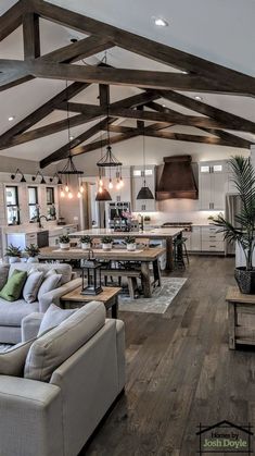 a living room filled with furniture and lots of wood beams on the ceiling over an open kitchen