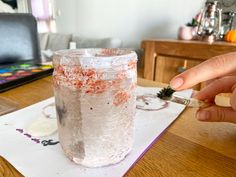 a person is holding a toothbrush in front of a jar on top of a table