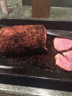 some meat is laying on a black tray with a knife and seasoning next to it