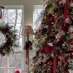 a christmas tree decorated with red and gold ornaments in front of two large window panes