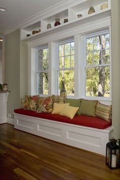 a window seat with pillows on it in front of two windows and a wood floor