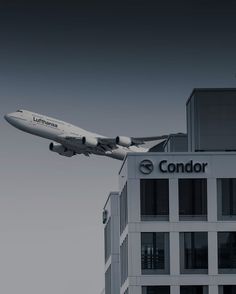 a large jetliner flying over a tall building next to a tall white building with the word condor on it's side