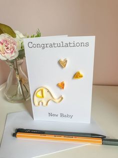 congratulations card with two elephants and hearts on it next to a pen, flower vase and pencil