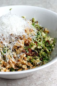 a white bowl filled with food and topped with parmesan cheese, nuts, and broccoli