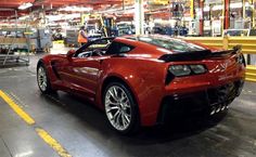 a red sports car is parked in a large warehouse with workers working on the assembly line