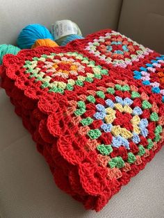 a crocheted blanket sitting on top of a couch next to balls of yarn