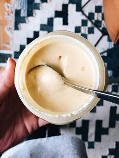 a person is holding a spoon in a jar with cream on the top and some sort of substance inside