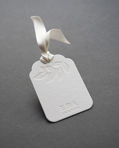 a white tag with a ribbon hanging from it's side on a gray surface