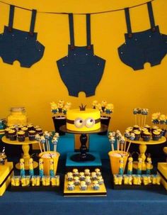 a yellow and blue dessert table with cupcakes, cake and decorations on it