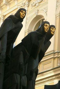 three black statues with gold faces are standing in front of a white and beige building