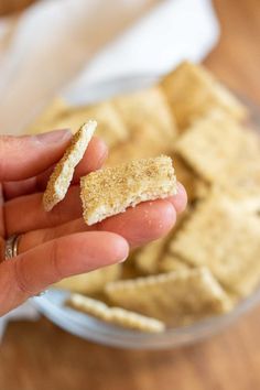 a hand holding some crackers in front of a bowl full of dip and pita chips