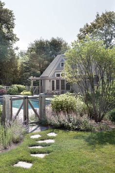 a garden with stepping stones leading to a pool in the background and a house on the other side