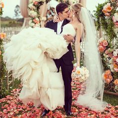 a bride and groom kissing in front of an archway with flowers on the ground at their wedding