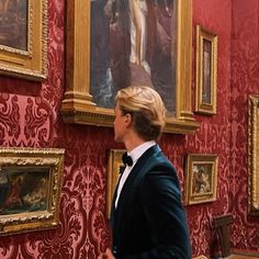 a man in a tuxedo is looking at paintings on the wall with red damask