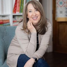 a woman sitting on a couch smiling at the camera with her hand under her chin