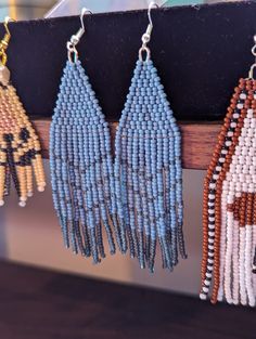 four beaded earrings hanging from a hook on a wooden rack in front of a window