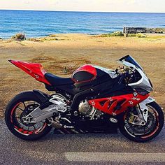 a red and black motorcycle parked in front of the ocean