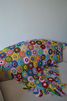 a multicolored crocheted blanket sitting on top of a white couch next to a wall