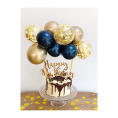 a birthday cake with gold and blue balloons on it, sitting on top of a table