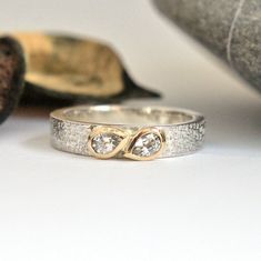 two wedding rings sitting next to each other on top of a white table with an object in the background