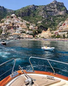 a boat traveling on the water near a city with mountains in the backgroud