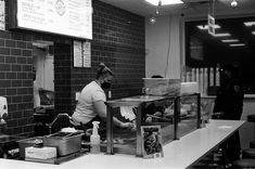 black and white photograph of a woman preparing food in a restaurant kitchen with people standing around