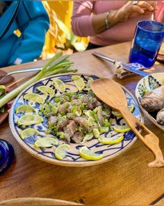 two plates with food on them sitting on a table next to a blue glass and wooden spoon