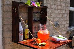 a wooden shelf with some drinks on top of it next to a brick wall and window