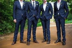 four men in suits are standing on a dirt road