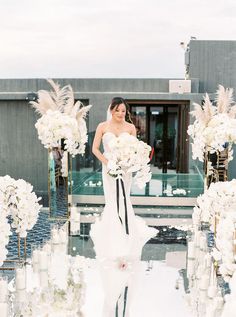 a woman in a white dress standing next to tall vases filled with flowers and candles