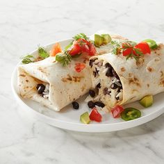 two burritos on a white plate with black beans and tomatoes