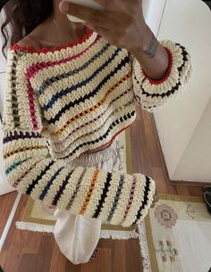 a woman taking a selfie while wearing a colorful crochet sweater and shorts