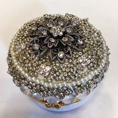 a silver box with pearls and jewels on it's lid is sitting on a white surface