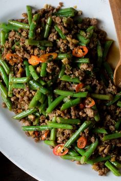 a white plate topped with green beans and ground meat next to a wooden serving spoon