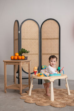 a baby sitting in a high chair next to two chairs with oranges on them