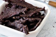 a white bowl filled with beef strips on top of a table next to a knife